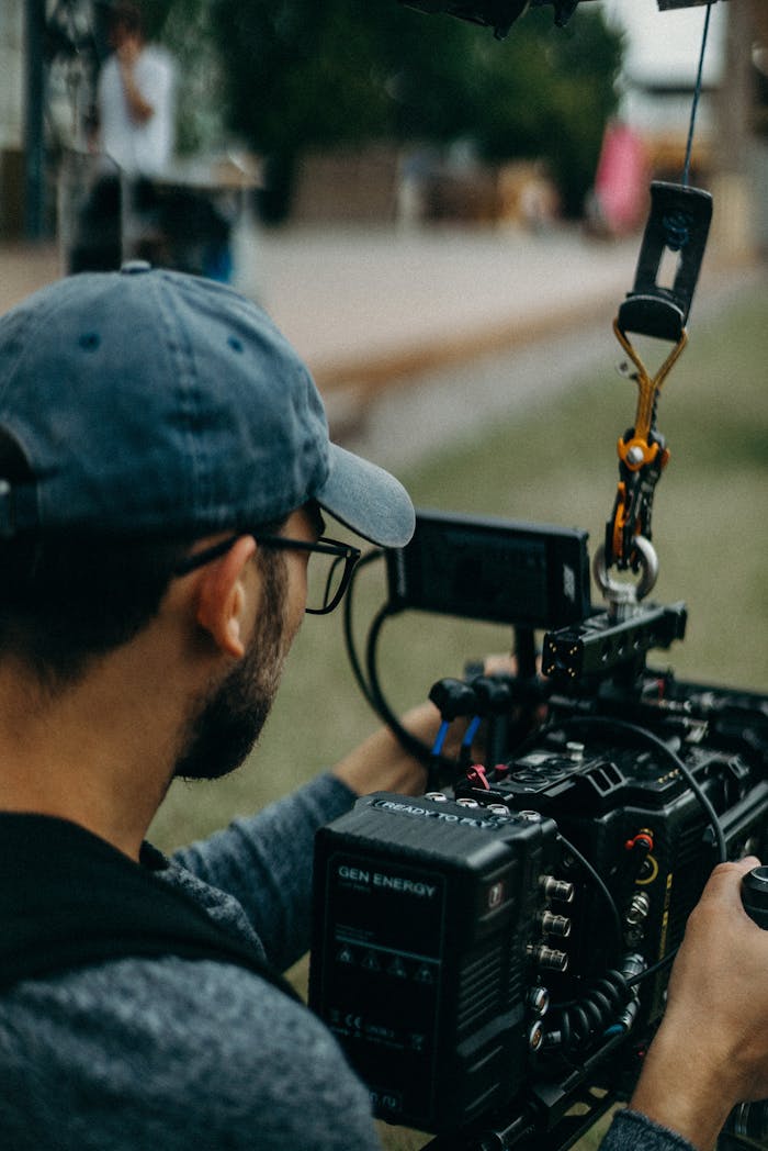 A focused filmmaker operating a cinema camera outdoors during daylight, capturing a creative video shoot.